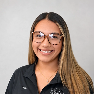 Chiropractic Assistant Chelsy Hernandez Smiling In Front Of Grey Background
