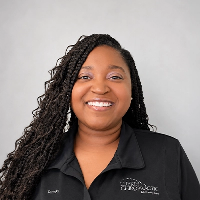 Back Office Manager Teneka Fowler Smiling In Front Of Grey Background